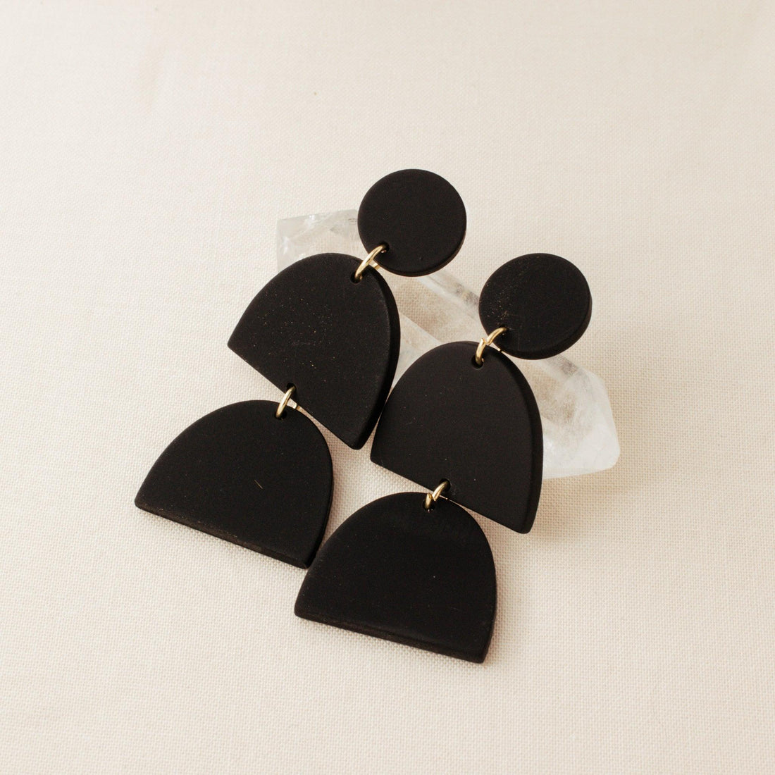Black polymer clay drop earrings by Avante Jewel laying on a clear crystal 