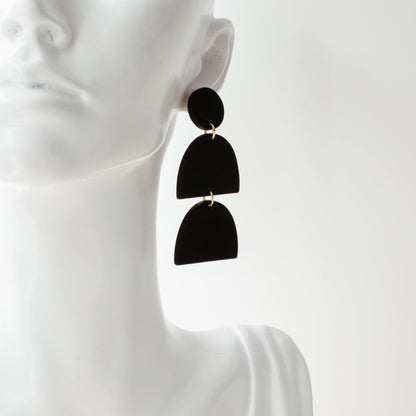 Black polymer clay drop earrings by Avante Jewel laying on a white mannequin