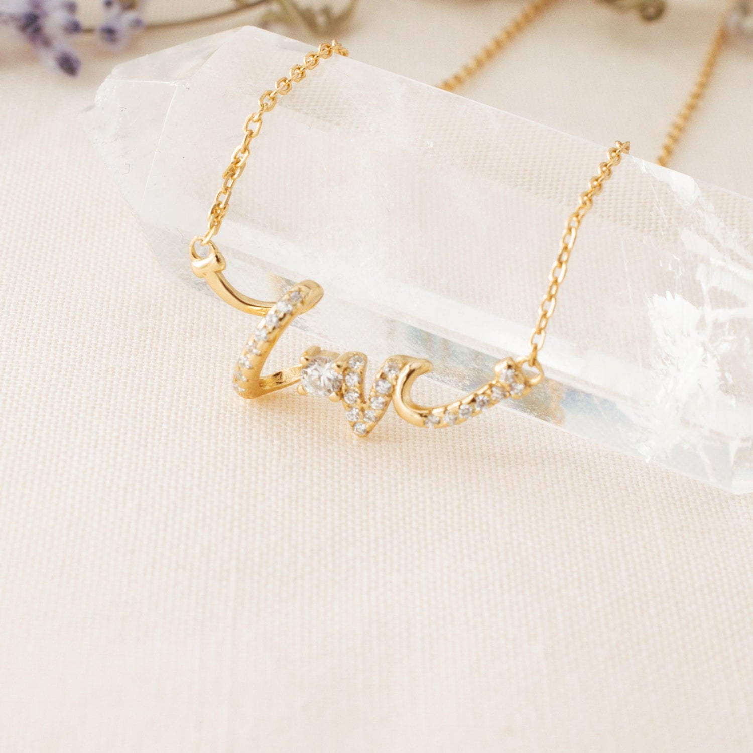 love pendant necklace laying on a crystal on cream background